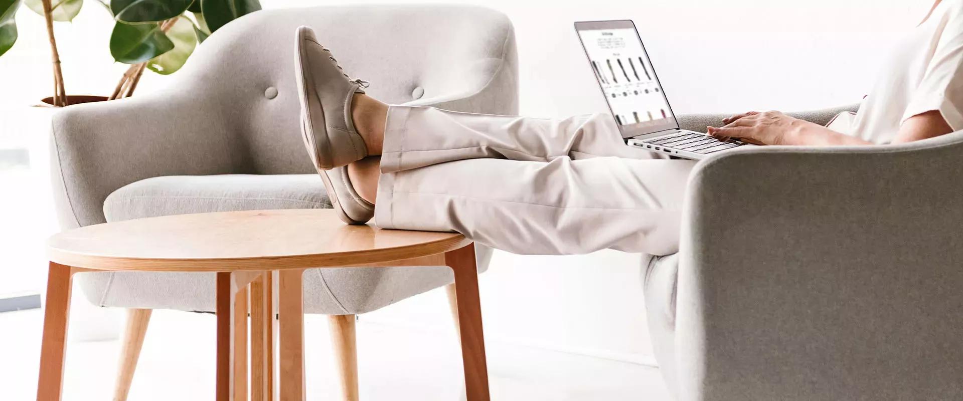 4 Tipps gegen geschwollene Beine Person sitzend mit Computer auf dem Schoß auf dem Sofa mit Füßen auf dem Tisch